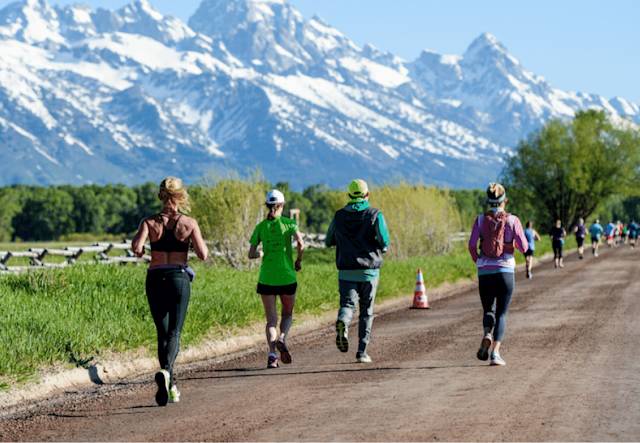 Four runners participating in a Vacation Races event on a road with mountains in the background.