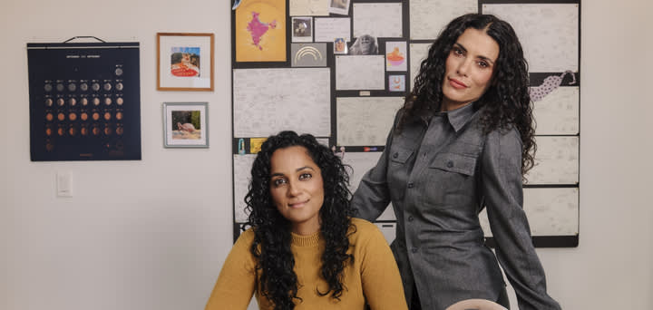 The CHANI co-founders pose in their office. Sonya Passi sits at the desk, and Chani Nicholas stands behind her with her hand on the back of the chair. In the center of the desk is a "2024 Inc. Best Workplaces" award.