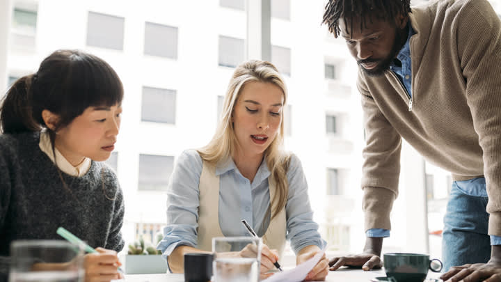 Three people taking notes in a conference room