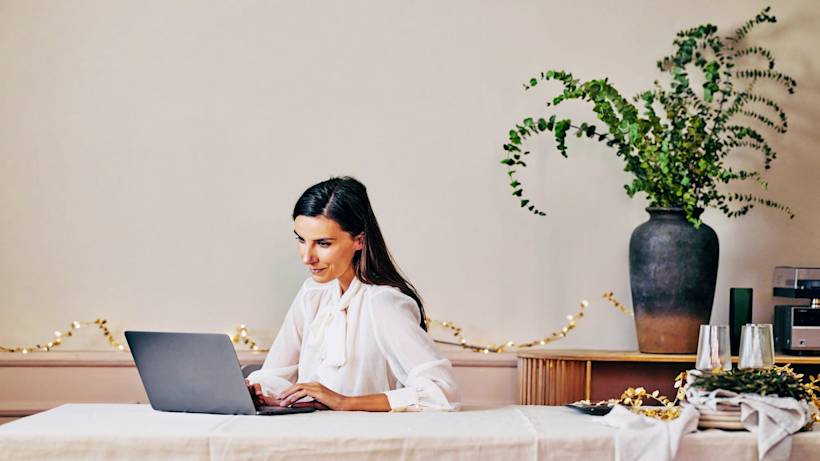 A woman works on her laptop in a chic, minimal setting with white holiday lights