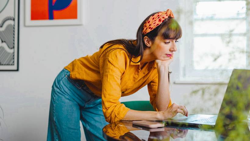 A young woman wearing a head bandana in a creative setting works on her laptop