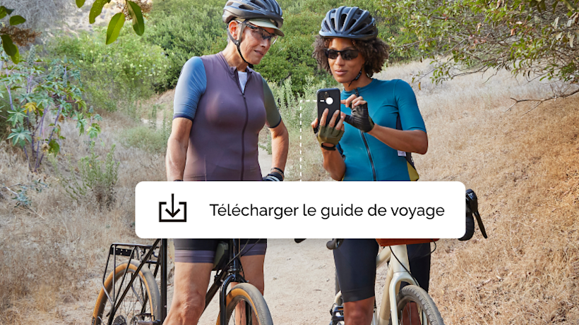 Deux femmes faisant une promenade à vélo, marquant une pause pour télécharger une application de guide de voyage offerte par une campagne Mailchimp.