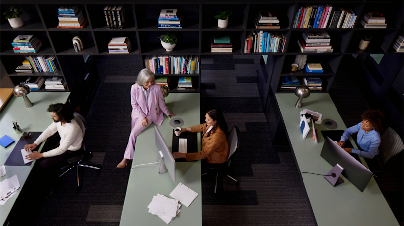 A group of people working at their desks, while their leader chats with one of them about the company’s automation strategy.